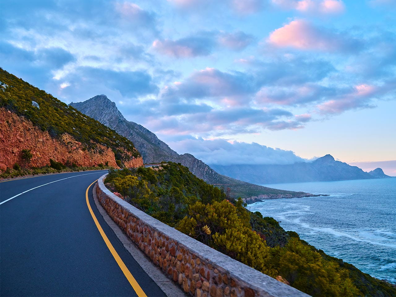 Coastal road curves by a rocky mountain and ocean.